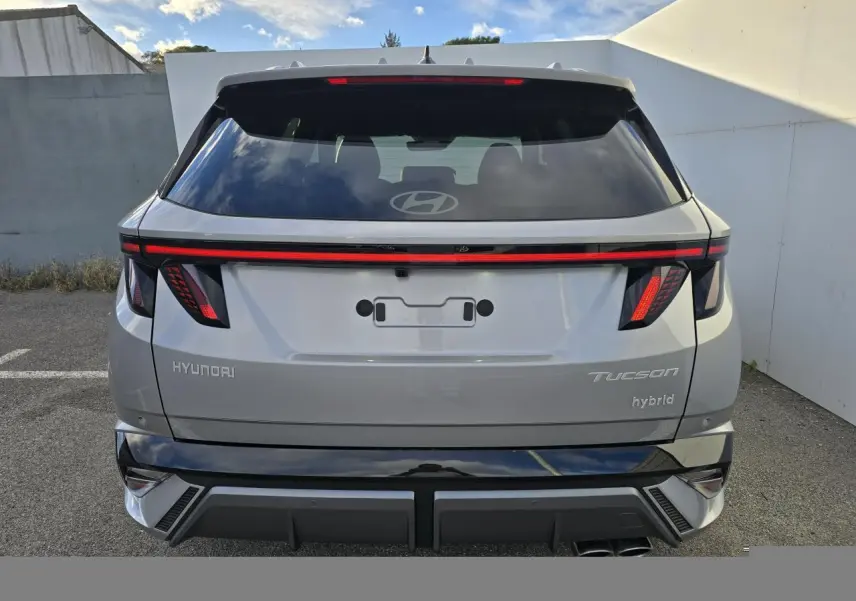Vue arrière d'un Hyundai Tucson hybride 2025 en argent métallisé avec feux arrière LED et double sortie d'échappement.