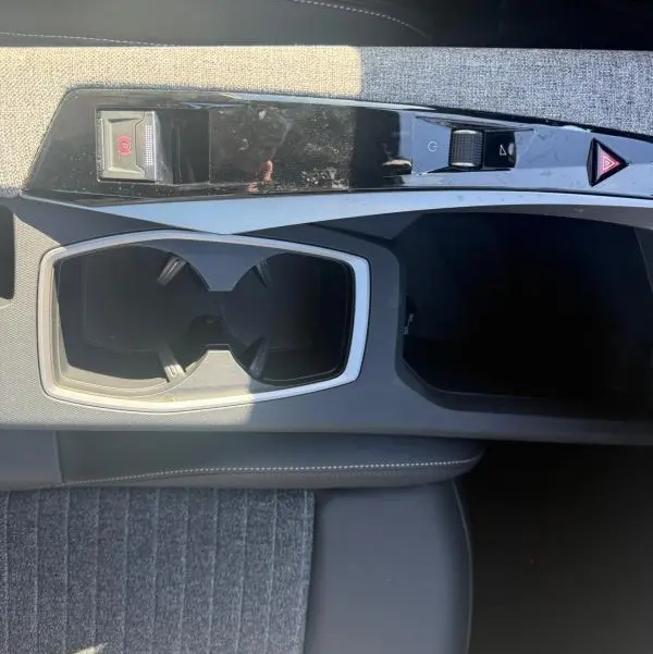 Vue plongeante sur la console centrale grise du Peugeot 3008 Hybrid 145 Allure, avec porte-gobelets et commandes de frein à main électrique.