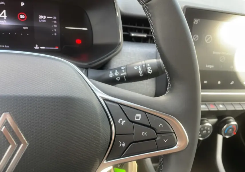 Gros plan sur le volant multifonctions de la Renault Clio gris schiste, avec tableau de bord numérique et commandes intégrées.