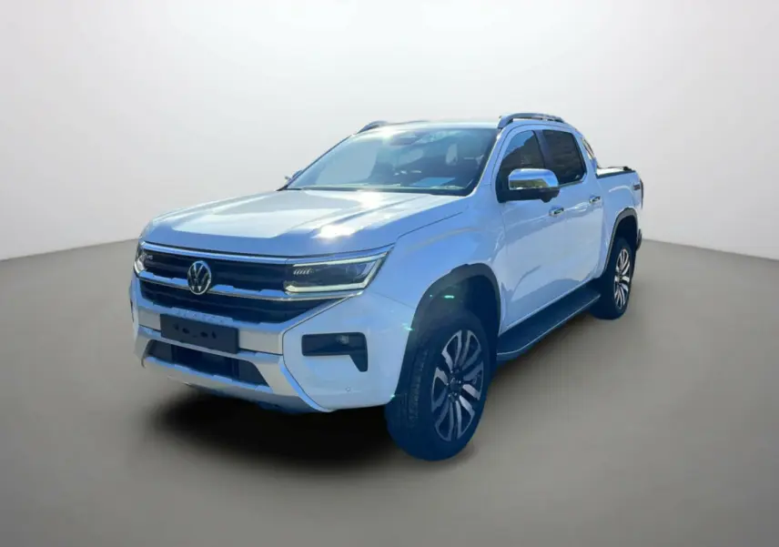 Volkswagen Amarok V6 blanc en 3/4 avant droit avec jantes alu 21 pouces et barres de toit visibles.