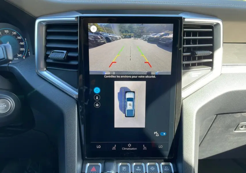 Vue rapprochée de l’écran central tactile du Volkswagen Amarok blanc, affichant la caméra 360° et les réglages de climatisation.