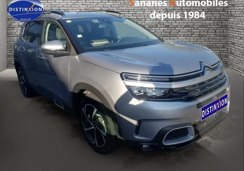 Vue 3/4 avant d'un Citroën C5 Aircross gris métallisé avec jantes alliage et barres de toit bi-ton.