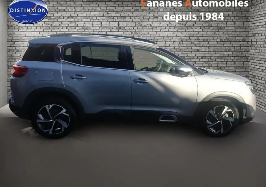 Profil côté gauche d’un Citroën C5 Aircross gris métallisé 2019 avec jantes alliage et barres de toit bi-ton.
