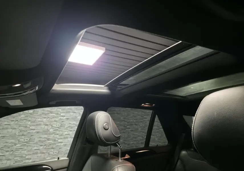 Toit ouvrant panoramique ouvert vu de l'intérieur arrière d'un Mercedes GLE 350 d gris clair avec sièges en cuir noir.