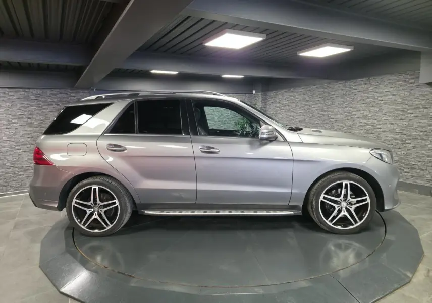 Vue latérale droite d'un Mercedes GLE 350 d gris clair avec jantes AMG 21 pouces et marchepieds inox en intérieur showroom.