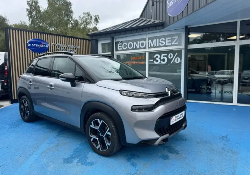 Citroën C3 Aircross gris acier vue 3/4 avant droit, toit noir et jantes alu distinctives, stationnée devant un showroom.