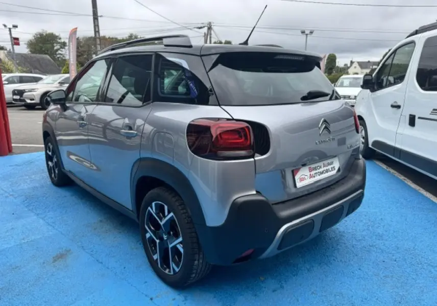 Vue 3/4 arrière droite d'une Citroën C3 Aircross gris acier avec barres de toit et jantes alu noires.