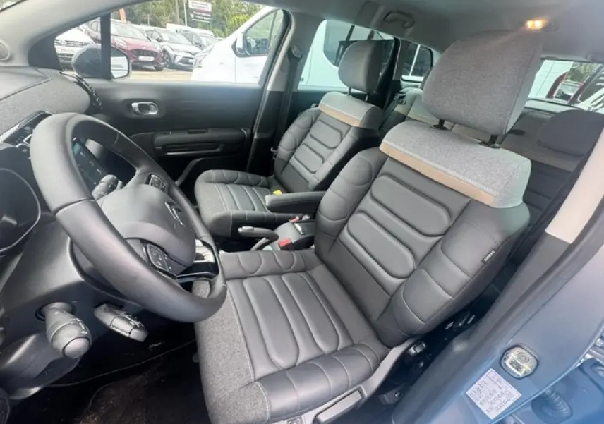 Vue intérieure côté conducteur de la Citroën C3 Aircross 2024, sièges bi-matière gris avec volant cuir noir.