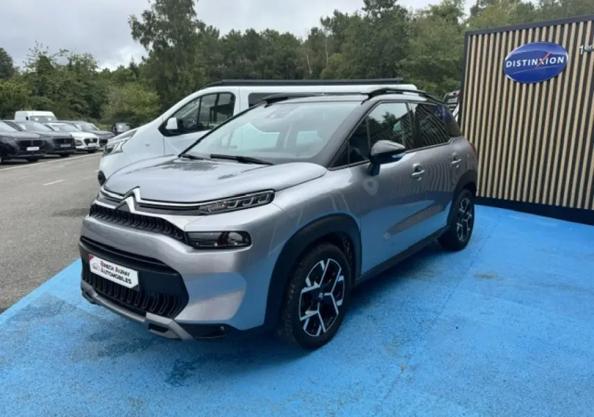 Citroën C3 Aircross gris acier vue 3/4 avant droit, avec barres de toit et jantes alu distinctives.