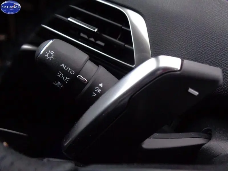 Gros plan sur la commande des phares et la palette de changement de vitesse dans l’habitacle noir du Peugeot 3008 Gris Artense.