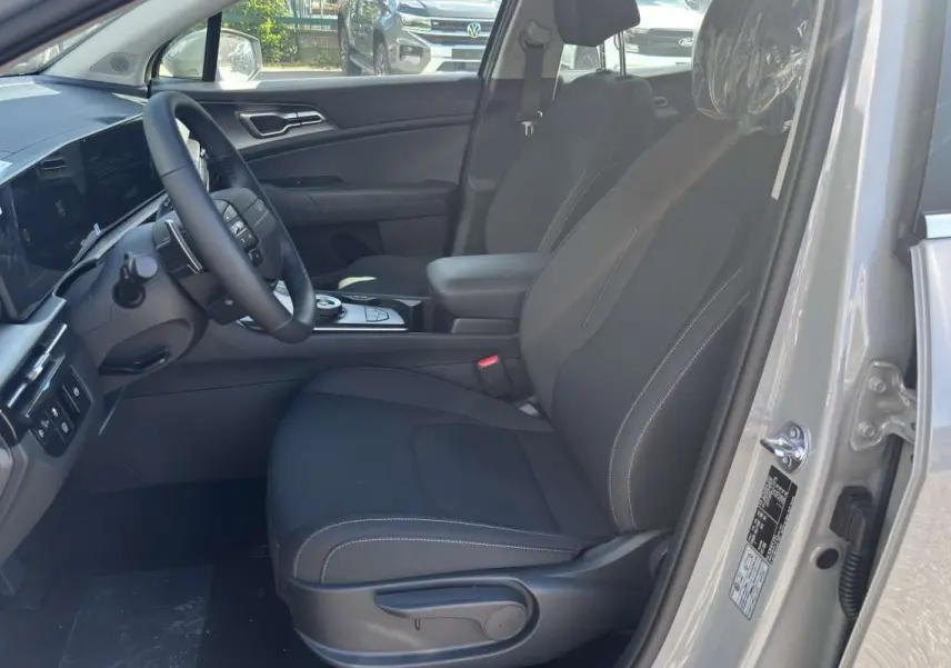 Vue intérieure côté conducteur du Kia Sportage gris céramique 2026, avec sièges tissu noirs et volant cuir multifonctions.