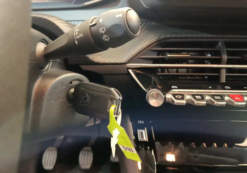 Gros plan sur le tableau de bord noir et la clé insérée dans le contacteur d'une Peugeot 208 gris foncé, version essence manuelle.