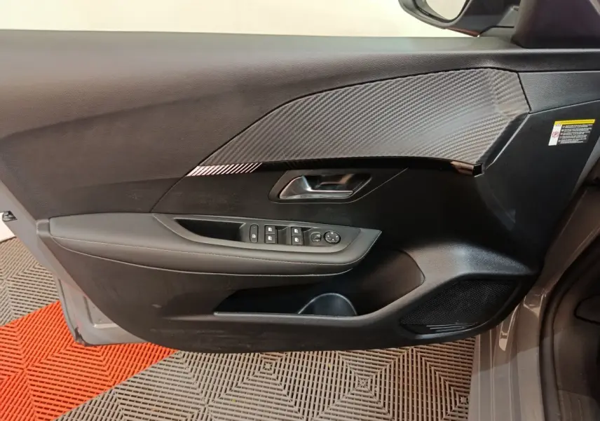 Vue côté gauche de la porte avant gris foncé du Peugeot 208 PureTech 100 S&S Allure avec commandes des vitres et décor carbone.