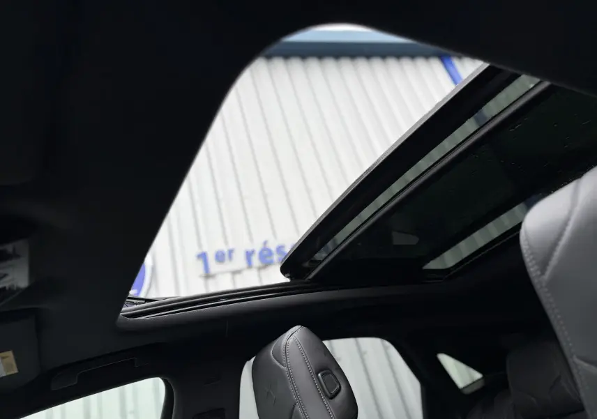 Vue intérieure du toit ouvrant électrique du DS7 gris titane, avec sièges avant en cuir visibles.