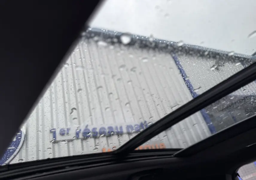 Vue intérieure du toit ouvrant électrique du DS7 gris titane avec gouttes de pluie visibles sur le verre panoramique.
