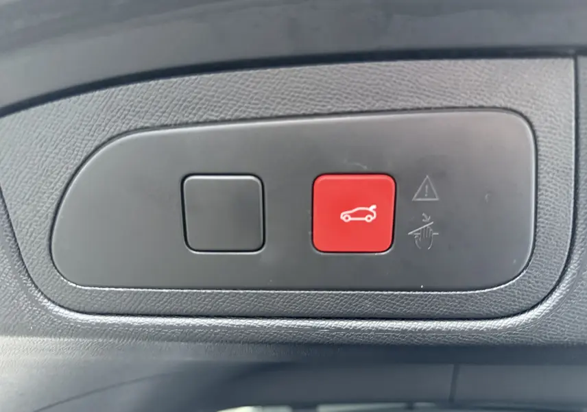 Gros plan sur le bouton rouge d'ouverture électrique du coffre dans l'habitacle du DS7 gris titane.