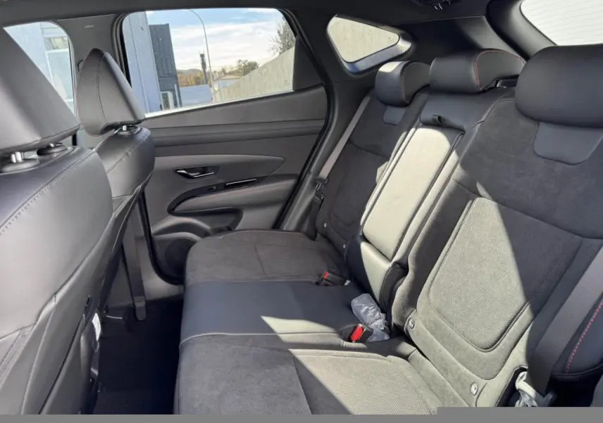 Vue intérieure arrière côté droit du Hyundai Tucson 2025 avec sellerie cuir/alcantara noire et surpiqûres rouges.