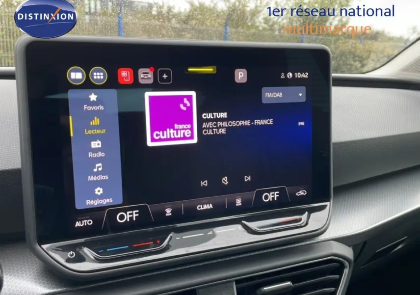 Vue rapprochée de l’écran tactile central du tableau de bord du SEAT LEON 2.0 TDI bleu Fjord, affichant une radio FM.