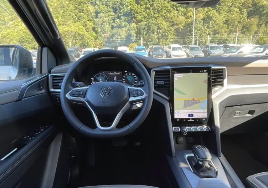 Vue intérieure avant du Volkswagen Amarok blanc 2026, tableau de bord moderne avec écran tactile vertical et volant multifonctions.