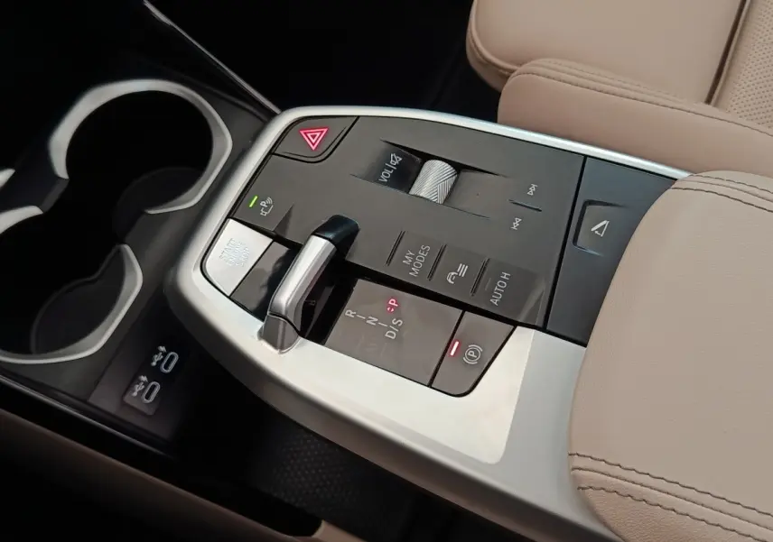Gros plan sur la console centrale beige du BMW X1 xDrive25e 2024 avec levier de vitesse et commandes tactiles.