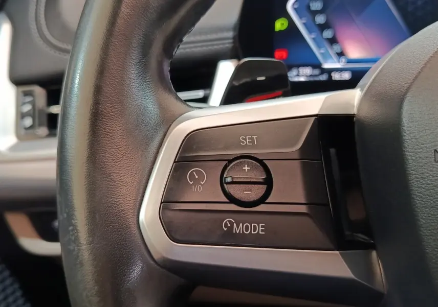 Gros plan sur les commandes du régulateur de vitesse au volant cuir noir du BMW X1 xDrive25e 2024.