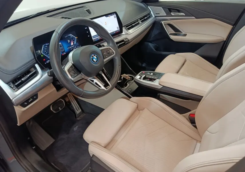 Vue intérieure côté conducteur du BMW X1 xDrive25e 2024 avec sièges cuir beige et tableau de bord digital moderne.