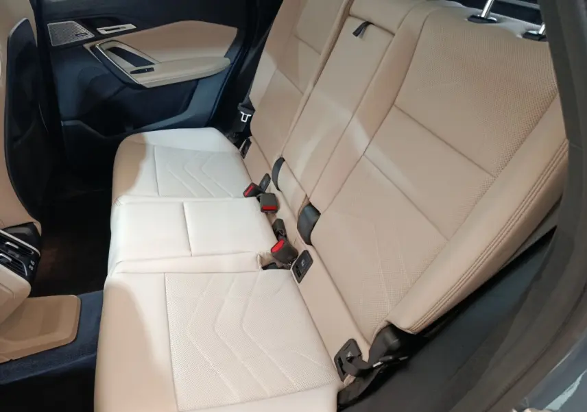 Vue intérieure sur la banquette arrière beige du BMW X1 xDrive25e M Sport 2024, avec ceinture et habillage gris foncé.