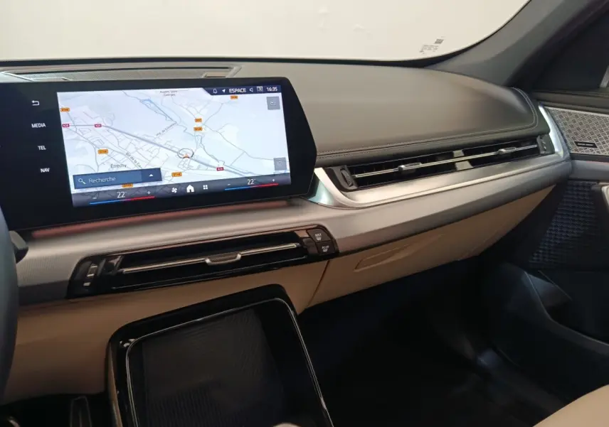 Tableau de bord beige et noir de BMW X1 xDrive25e M Sport 2024 avec écran tactile central affichant une carte.