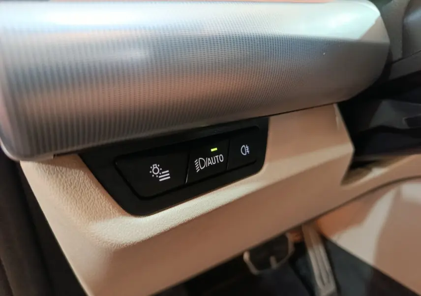 Gros plan sur les commandes d’éclairage automatiques intégrées au tableau de bord beige du BMW X1 xDrive25e M Sport 2024.