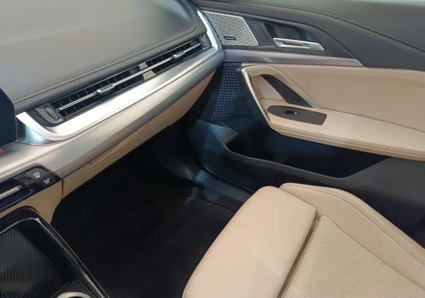 Intérieur avant droit du BMW X1 xDrive25e 2024, avec sellerie beige, tableau de bord noir et inserts aluminium.