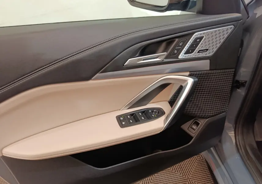 Vue intérieure côté gauche de la porte BMW X1 xDrive25e M Sport 2024, garniture beige et noire avec commandes électriques.