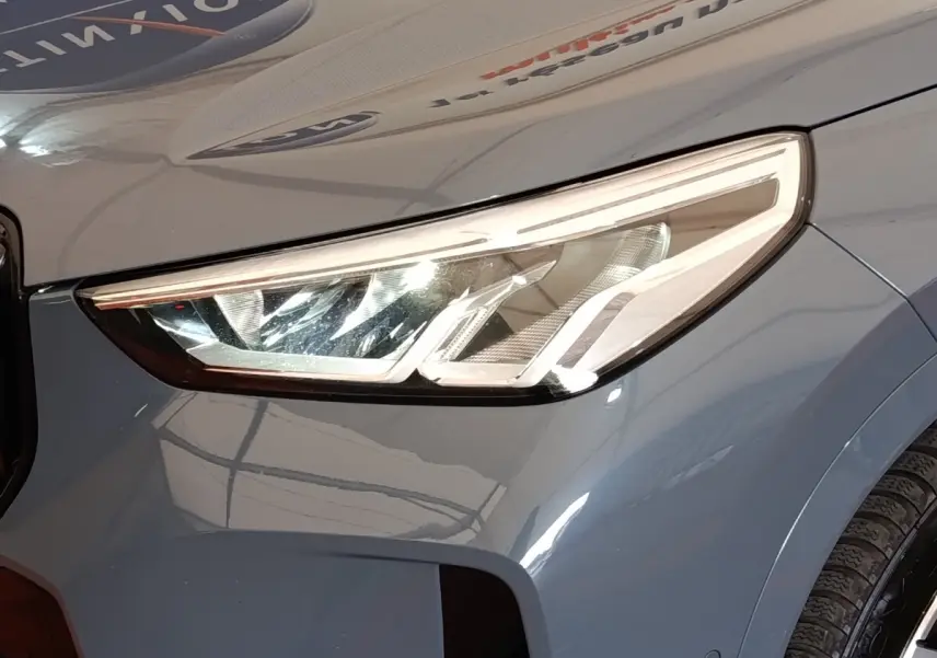 Gros plan sur le phare avant droit d’un BMW X1 xDrive25e M Sport gris foncé 2024 avec peinture métallisée.