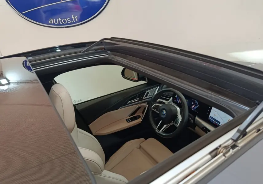 Vue intérieure par le toit ouvrant d'une BMW X1 xDrive25e M Sport 2024 gris foncé, sièges cuir beige et tableau de bord digital.
