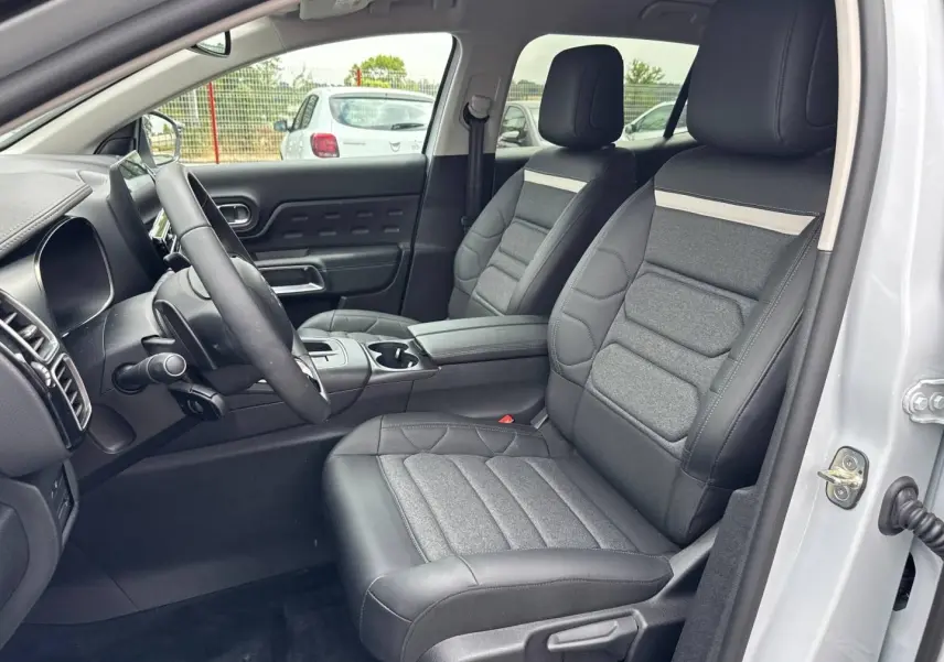 Vue intérieure côté conducteur du Citroën C5 Aircross blanc, sièges avant en tissu et cuir noir avec accoudoir central.