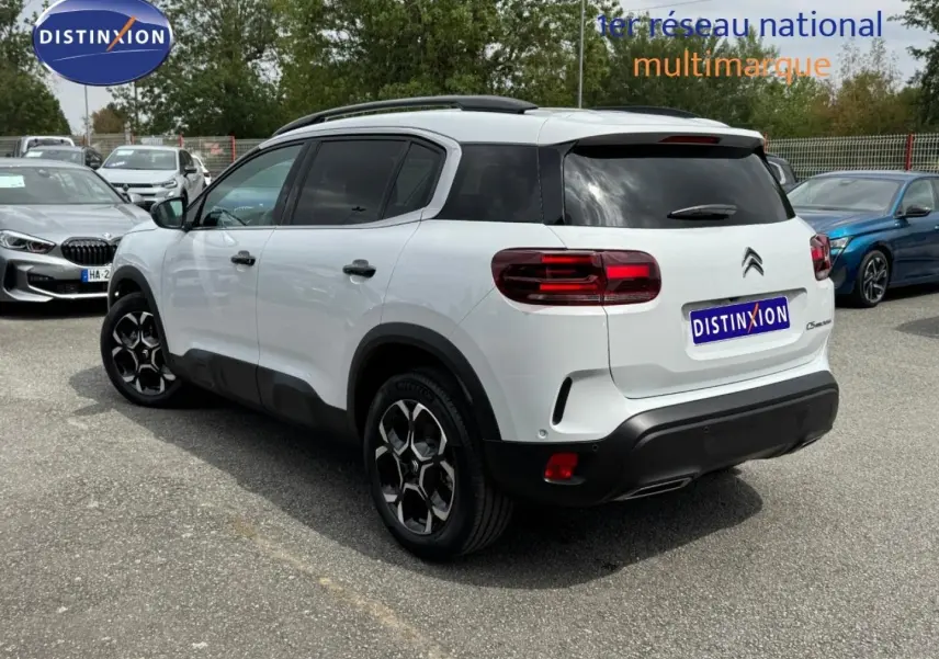 Vue 3/4 arrière droite d'un Citroën C5 Aircross blanc Okénite avec jantes alu et barres de toit noires.