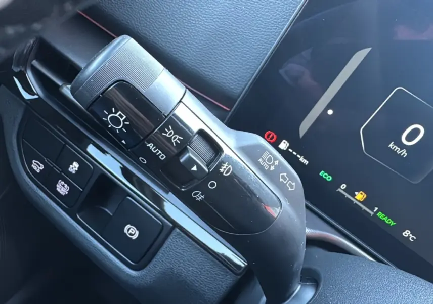 Détail du commodo d'éclairage et frein à main électrique dans l'habitacle du Kia Sportage 2026 noir étoilé.