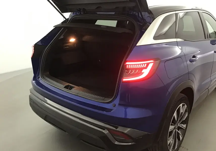 Vue 3/4 arrière droite du Renault Austral bleu Iron avec coffre ouvert et feux arrière allumés.