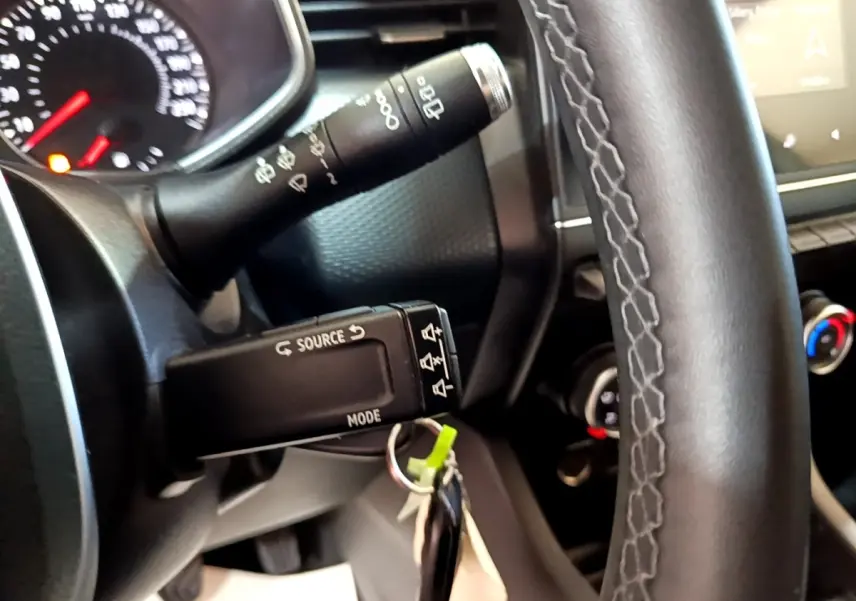 Gros plan sur le volant noir et la commande multimédia à gauche du tableau de bord intérieur d’une Renault Clio blanche.