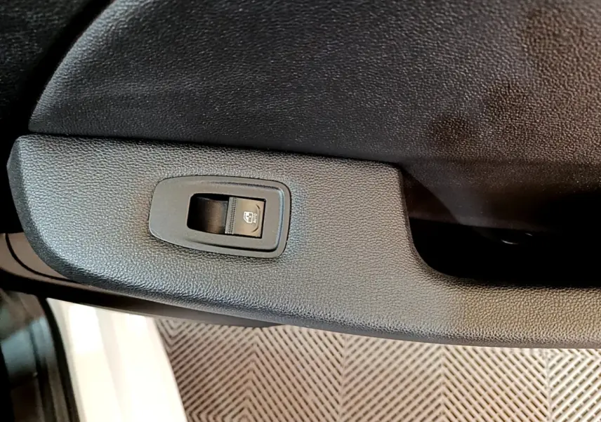 Gros plan sur le bouton de commande de la vitre électrique côté porte arrière d'une Renault Clio blanche.