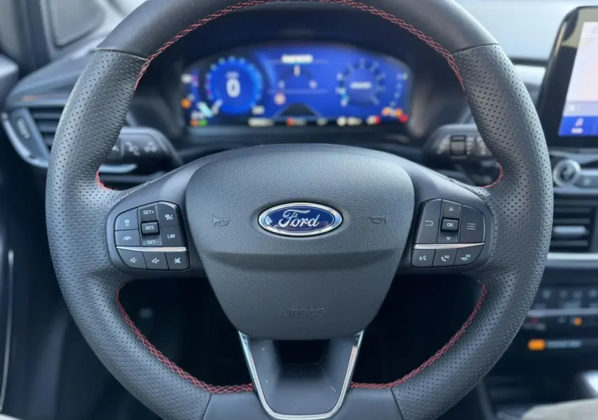 Vue rapprochée du volant perforé noir avec surpiqûres rouges et tableau de bord numérique du Ford Puma 2023.