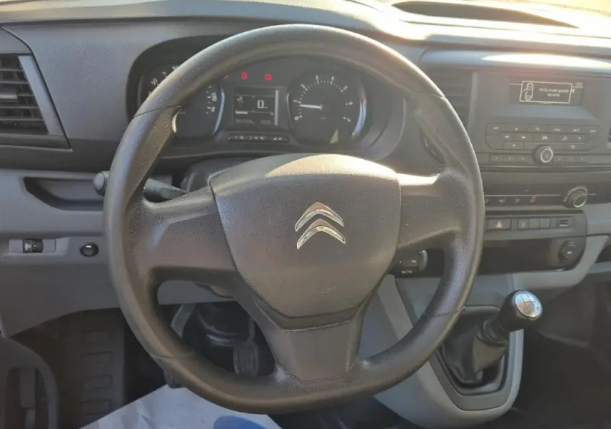 Vue intérieure centrée sur le volant noir et la console centrale du Citroën Jumpy blanc, boîte manuelle visible.