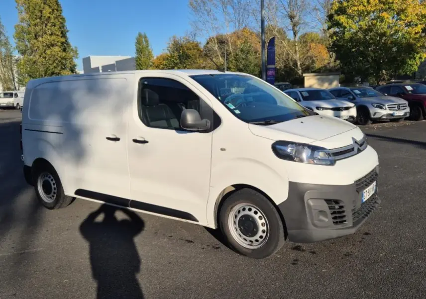 Vue 3/4 avant gauche d’un Citroën Jumpy blanc fourgon L1H1 avec pare-chocs noirs, stationné en extérieur.