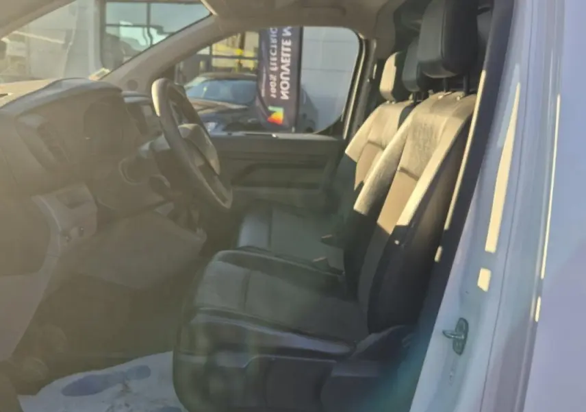 Vue intérieure côté conducteur du Citroën Jumpy blanc 2019, montrant les sièges avant en tissu et le tableau de bord simple.