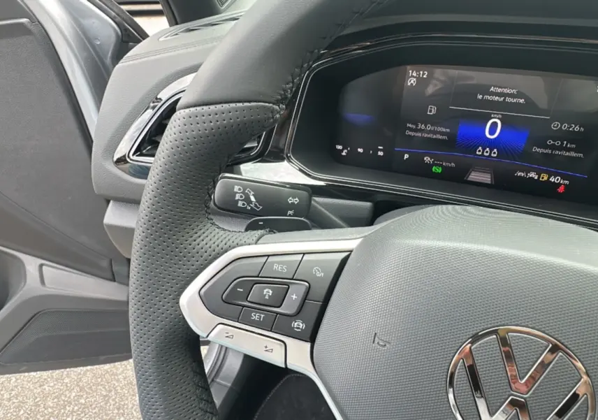 Gros plan sur le volant cuir perforé et le tableau de bord digital du Volkswagen T-Roc gris pyrite, version R-Line Black.