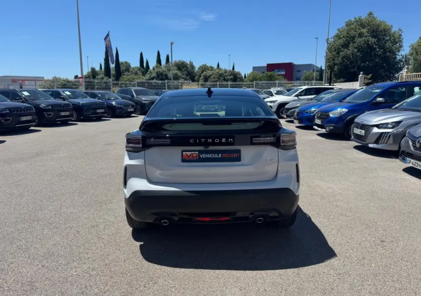 Vue arrière d'une Citroën C4 hybride blanche 2025 avec toit noir, feux LED et double sortie d'échappement.