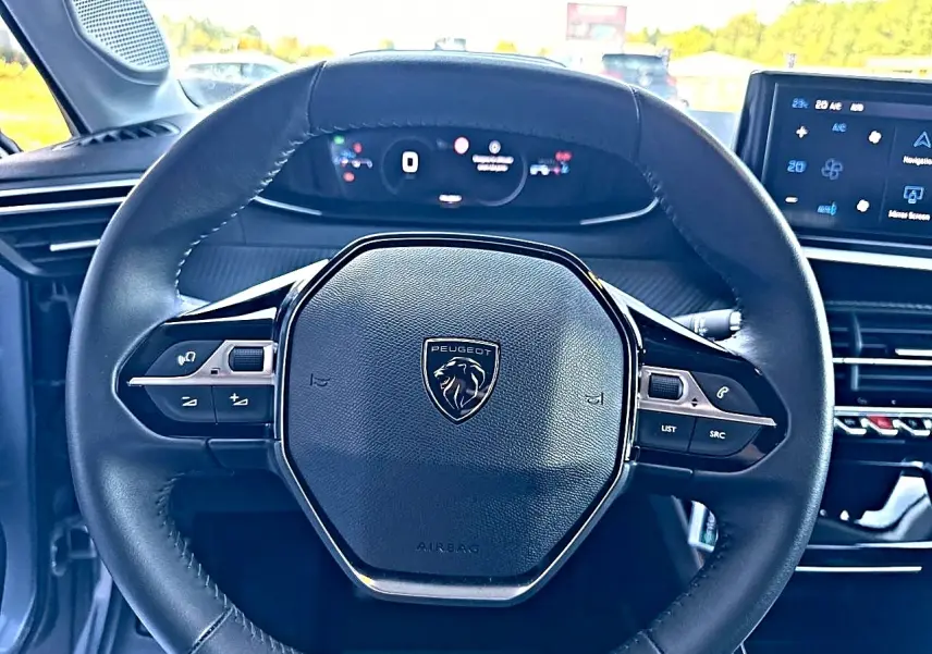 Vue rapprochée du volant cuir noir avec logo Peugeot, tableau de bord numérique et écran tactile du Peugeot 208 1.2 100 Allure.