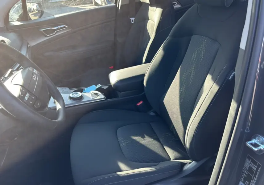 Vue intérieure côté conducteur du Kia Sportage gris eclipse 2026, sièges tissu noirs et volant cuir multifonctions.
