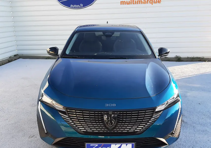 Vue frontale d'une Peugeot 308 2025 Bleu Obsession avec calandre noire et logo lion central, stationnée devant un mur blanc.