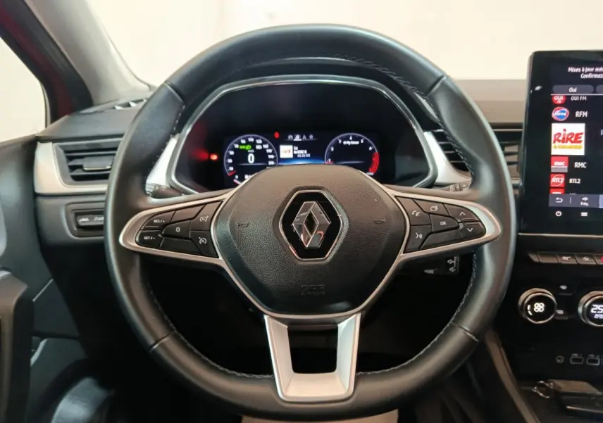 Volant noir Renault Captur 2024 avec commandes intégrées et tableau de bord numérique en arrière-plan.