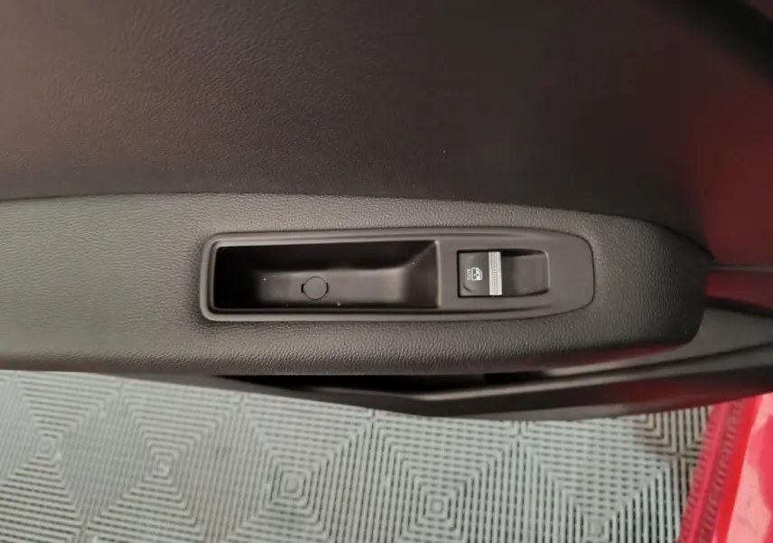 Poignée intérieure côté gauche de la porte du Renault Captur rouge 2024 avec bouton de commande de vitre électrique.